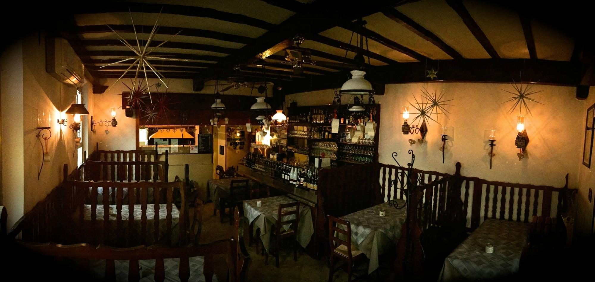 La sala de La Lanterna a lume di candela: travi di legno, lampade a stella in ferro battuto, pareti di bottiglie